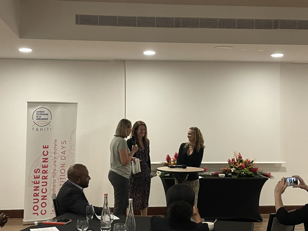 Three women talking to each other at the front of a room 